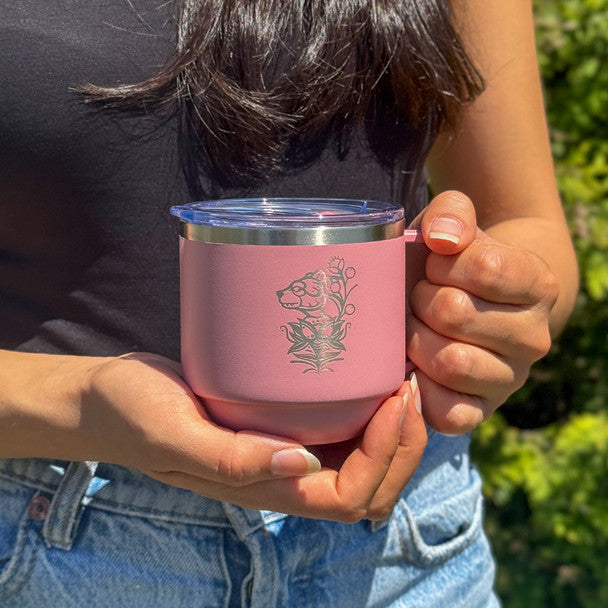 Person holding a pink insulated mug with a design outdoors