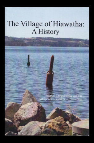 Book cover of 'The Village of Hiawatha: A History' with a scenic view of water and rocks.