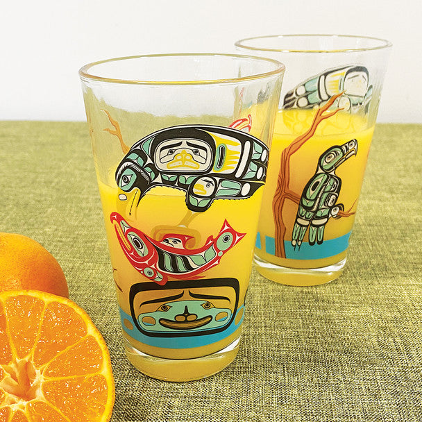 Two glass tumblers with Native American art designs on a green surface with oranges.