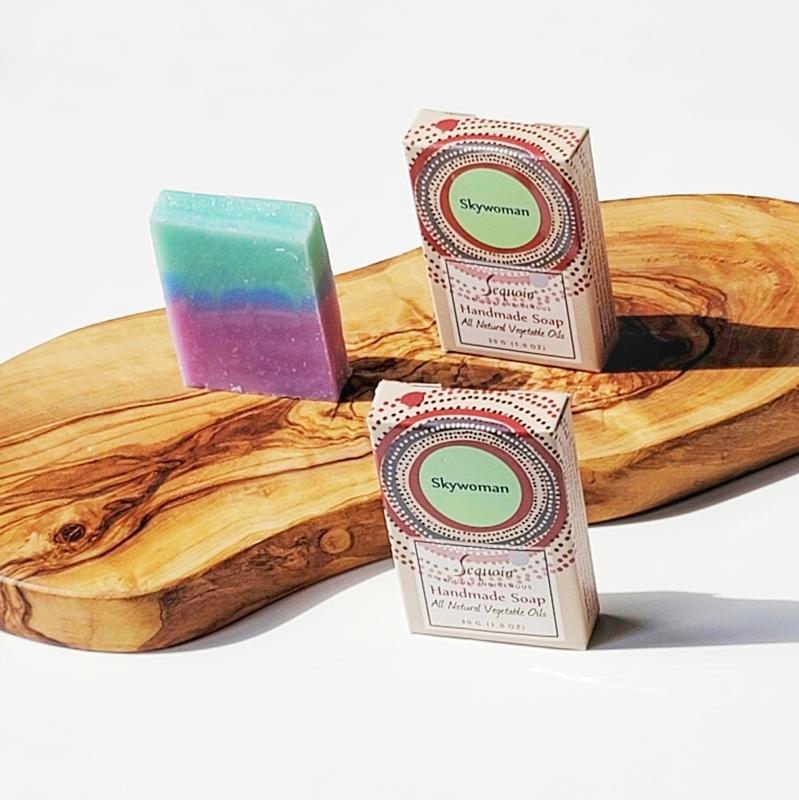 Two boxes of Skywoman soap on a wooden surface with a colorful bar of soap.