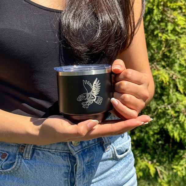 Person holding a black insulated mug with a design outdoors