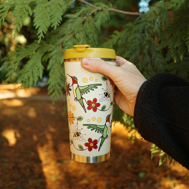Hand holding a colorful tumbler with nature-themed design against a forest background
