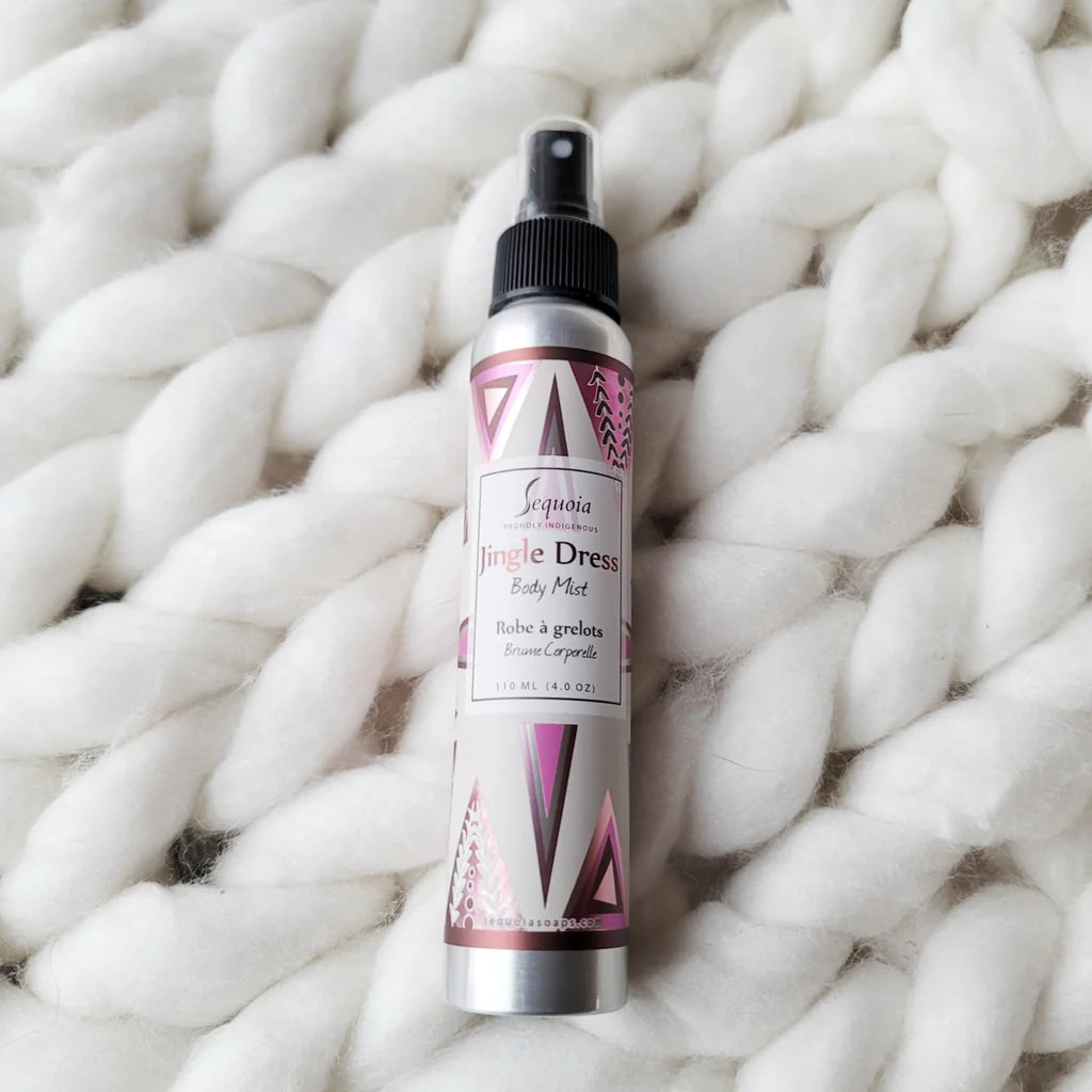 Body mist bottle with pink and white label on a textured white surface
