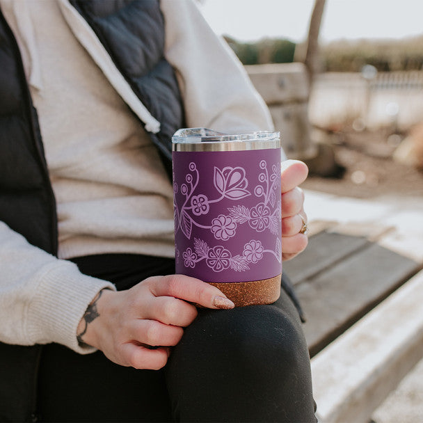 Person holding a purple insulated tumbler with floral patterns outdoors.