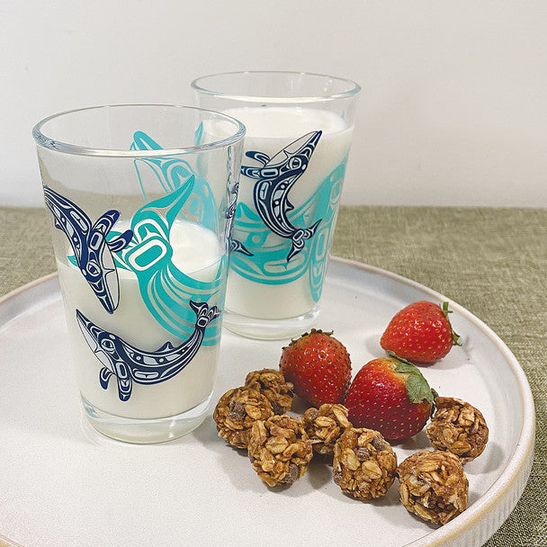 Two glasses with dolphin designs filled with milk, surrounded by strawberries and granola on a white plate.